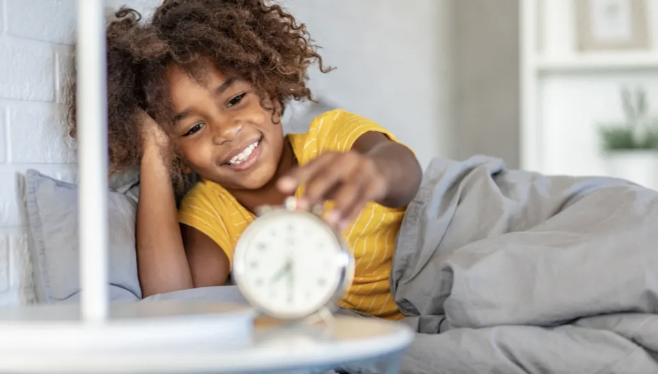 A CHILD TURNS OFF THEIR ALARM CLOCK WITH A SMILE.